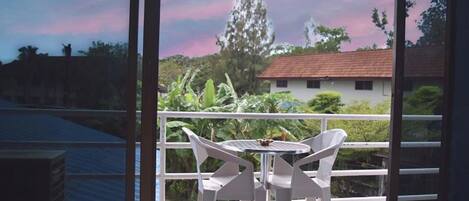 Uma varanda com mesa e cadeiras, com vista para um jardim e um edifício.