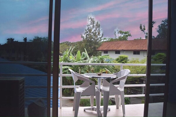 Un balcón con mesa y sillas, con vistas a un jardín y un edificio.