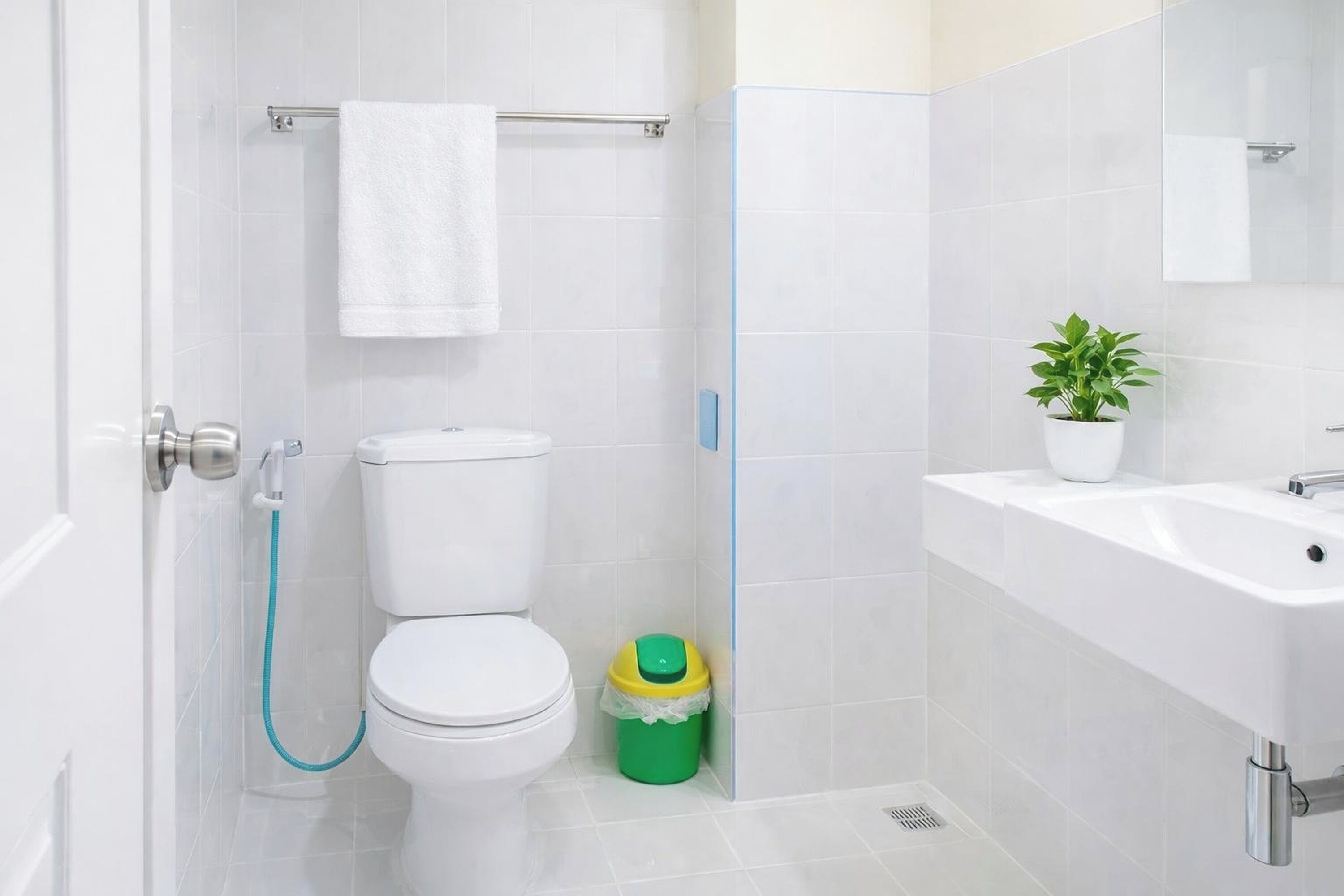 A bathroom with a toilet, a sink, and a green trash bin.