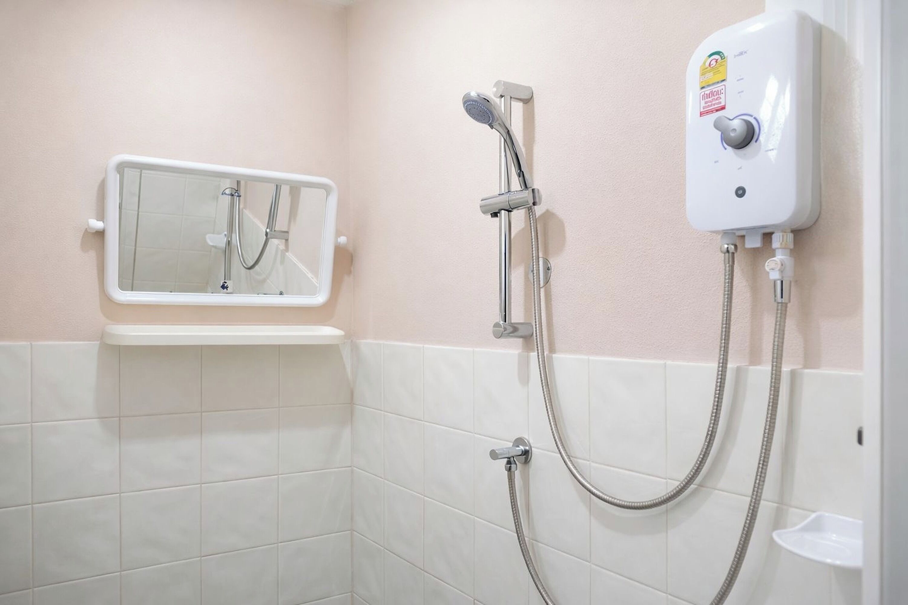 Une salle de bain équipée d’une douche, d’un pommeau de douche amovible, d’un panneau de commande fixé au mur et d’un miroir doté d’un cadre de sécurité.