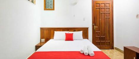 A hotel room with a large bed, a wooden headboard, a red throw, and a set of towels on the bed.