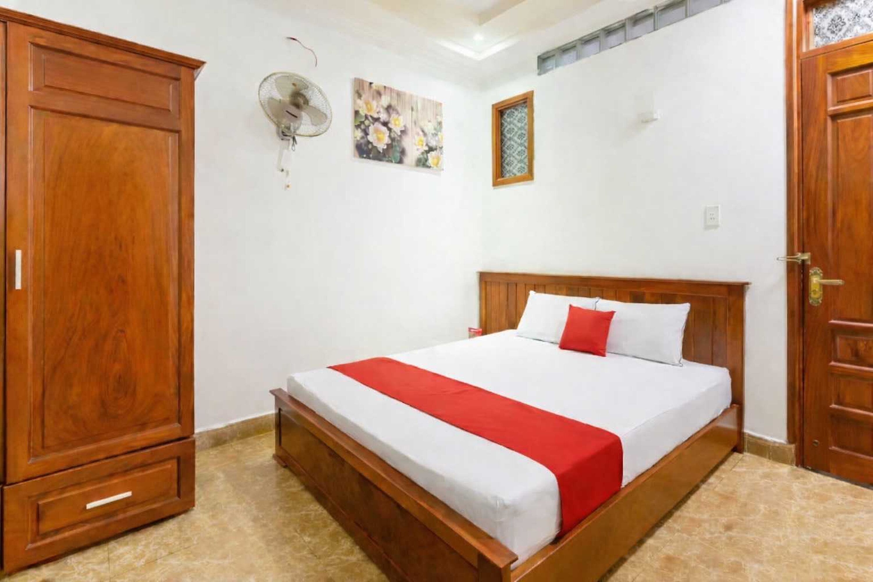 A bedroom with a wooden bed, a wardrobe, a wall-mounted fan, and a decorative picture.