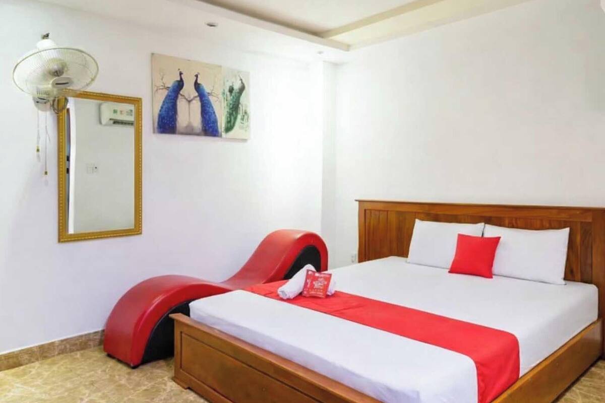 Une chambre à coucher avec un lit, une chaise rouge, un miroir et un tableau accroché au mur.
