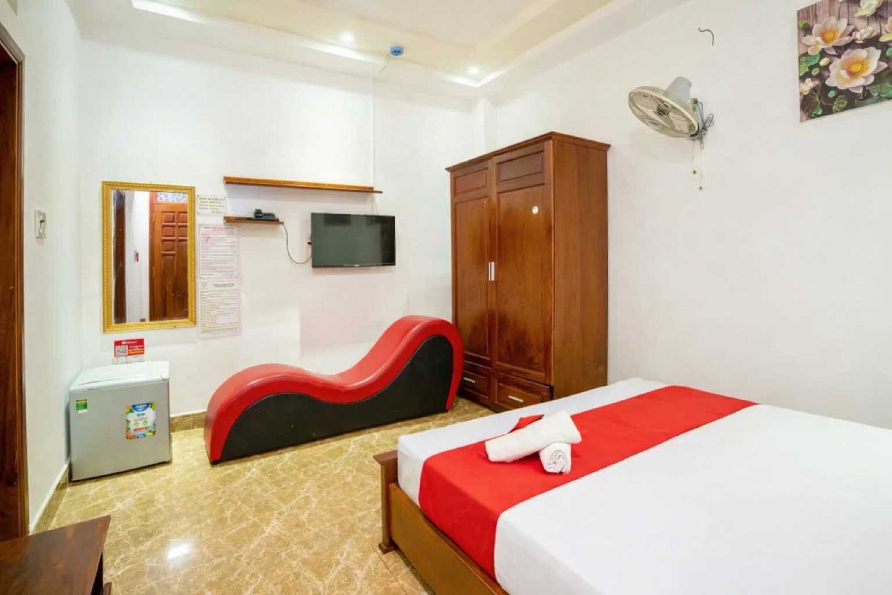 A hotel room with a bed, a TV, a wardrobe, a small fridge, and a red chair.