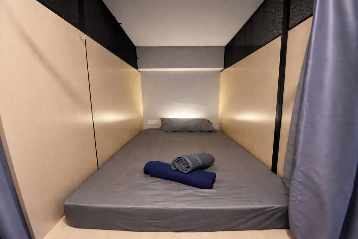 A small, narrow room with a single bed, a pillow, and a rolled towel.