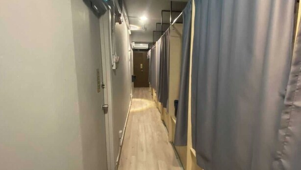 Un couloir étroit au plancher de bois, bordé de murs ornés de rideaux et avec une porte au bout.