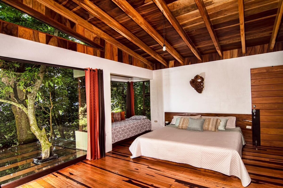 A bedroom with a large window, wooden ceiling beams, and a bed with multiple pillows.
