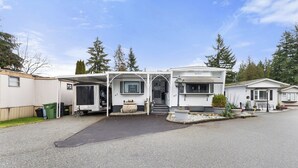 A row of white mobile homes with attached garages, a paved driveway, and a small garden area with plants and a bench.