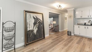 A modern kitchen with white cabinets, a wooden floor, and a framed artwork on the wall.
