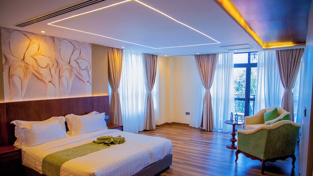 A hotel room with a large bed, a green armchair, and a view of the outdoors through the windows. - THE MAVVEL (Mutunduri)