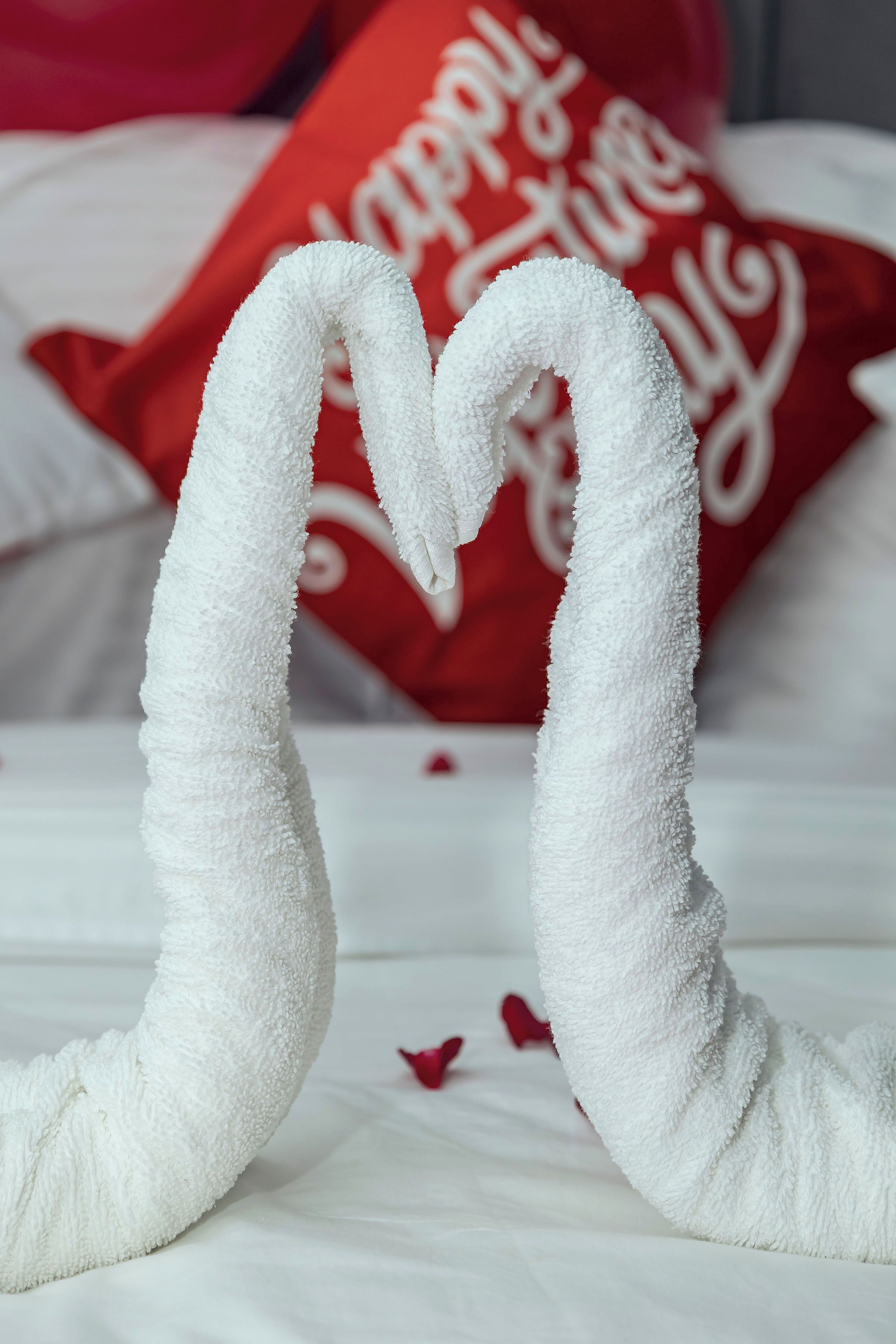 A bed with white sheets and a red pillow with white text.