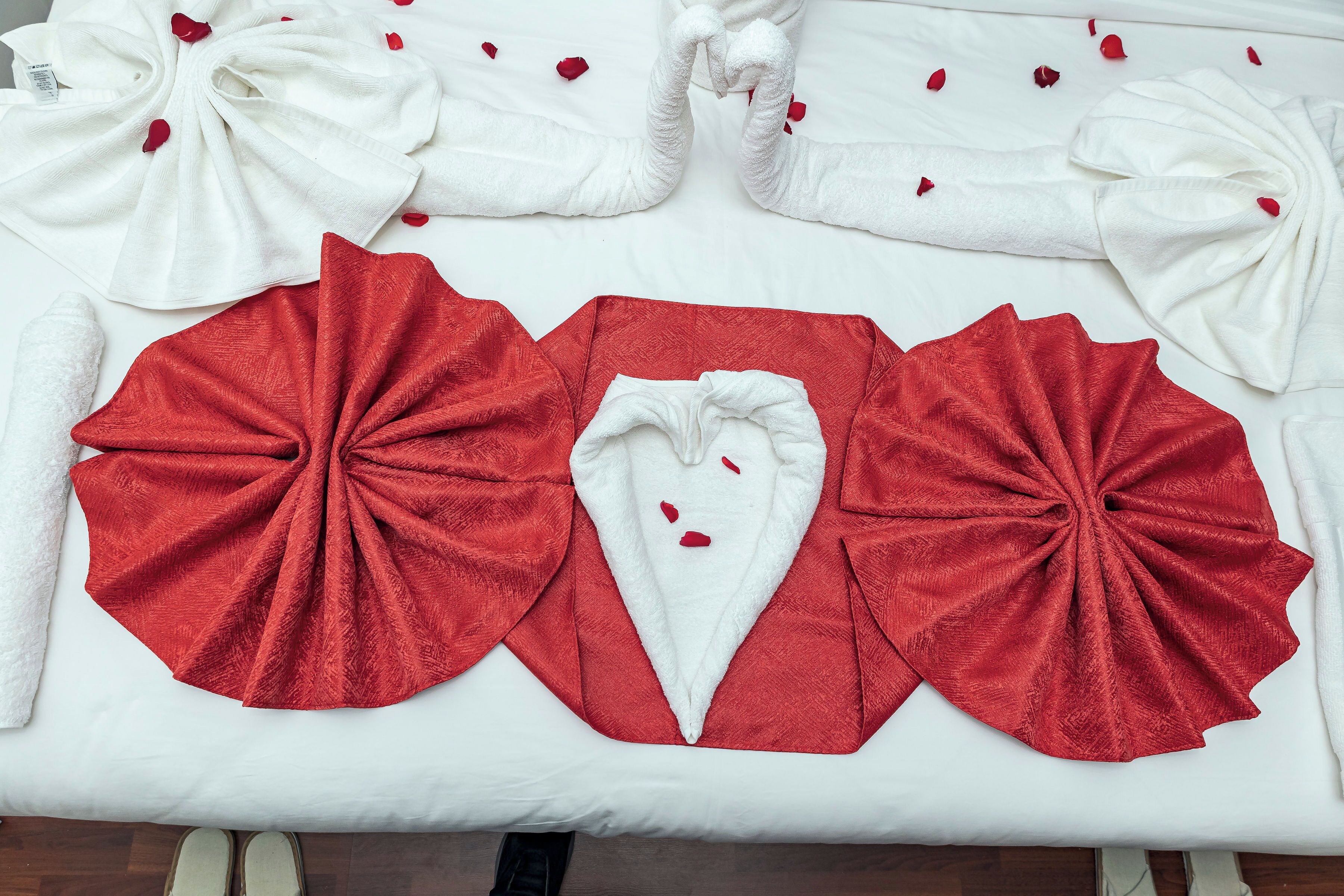 A neatly arranged set of towels and bathrobes on a bed, with red towels and white bathrobes.
