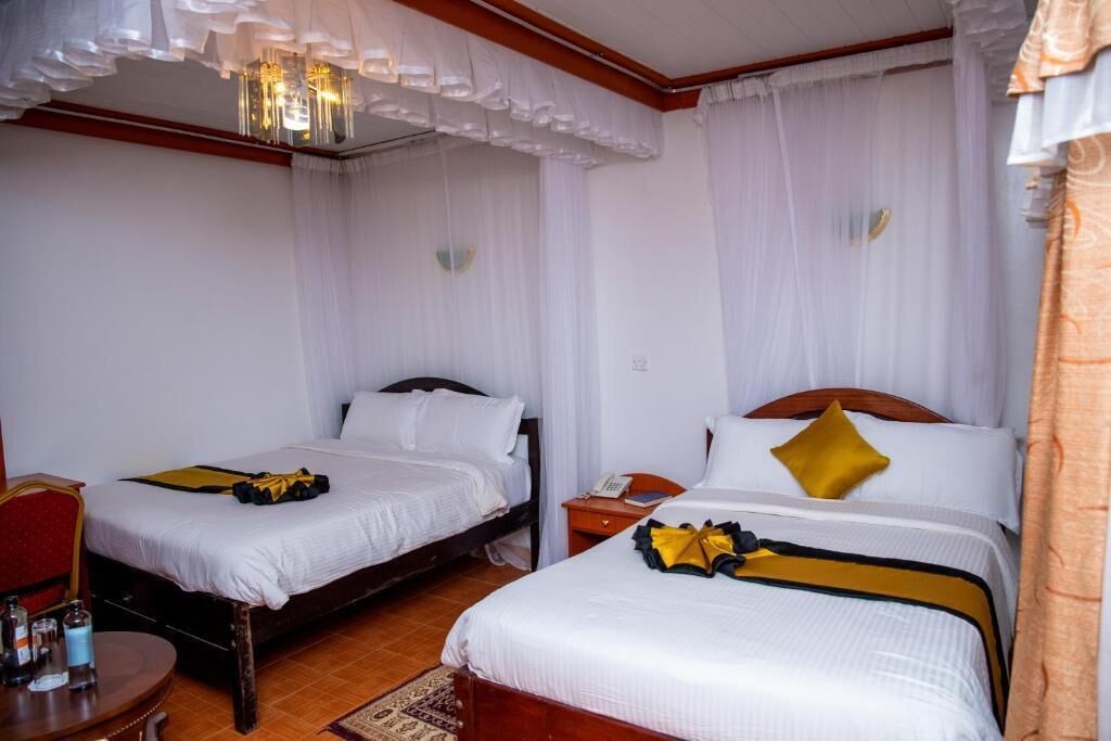 Une chambre d’hôtel avec deux lits, une tête de lit en bois, une petite table avec une chaise et un lustre.
