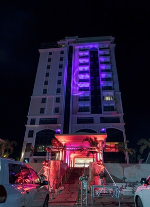 A multi-story hotel with a prominent entrance featuring a red-lit canopy and a staircase leading to the entrance. - THE MAVVEL (Mutunduri)