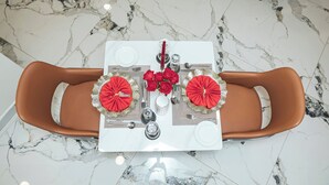 A dining table set with red and gold accents, surrounded by brown leather chairs, on a marble floor. - THE MAVVEL (Mutunduri)