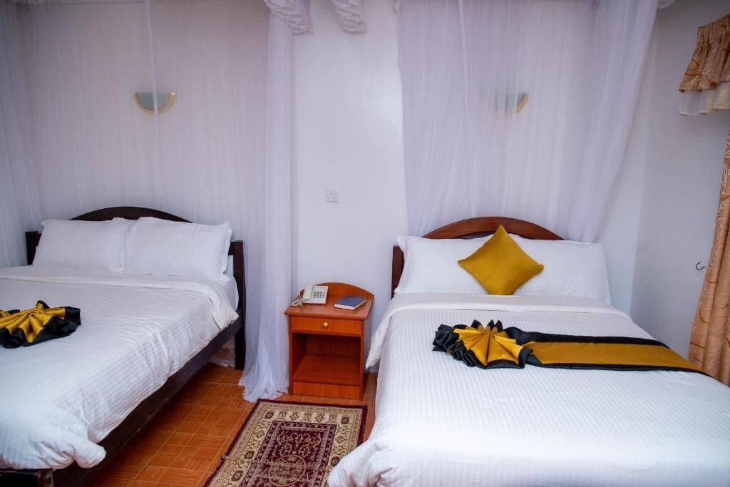 Habitación de hotel con dos camas individuales, una mesita de noche de madera, un teléfono y una alfombra decorativa.