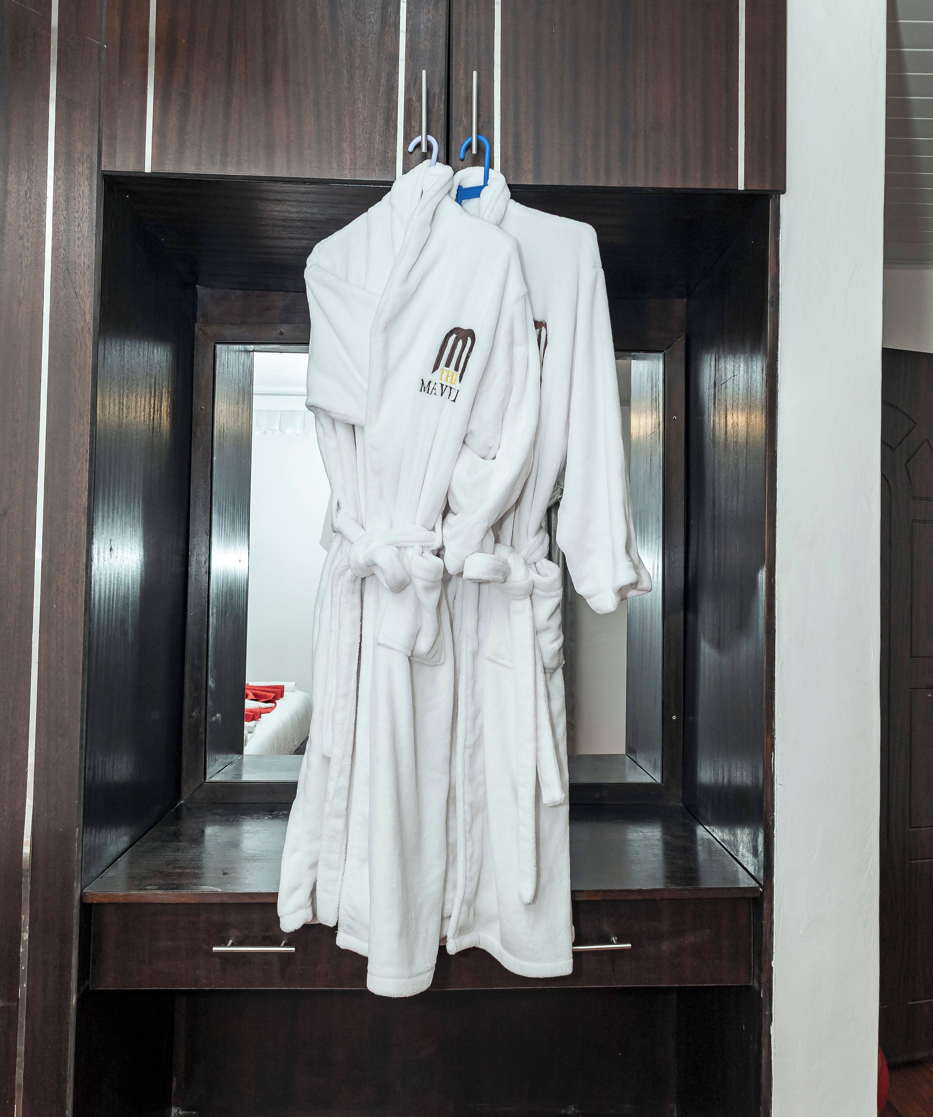A dark wooden wardrobe with white robes hanging on a rack.