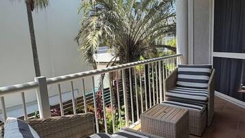 A balcony with wicker furniture and a view of palm trees.