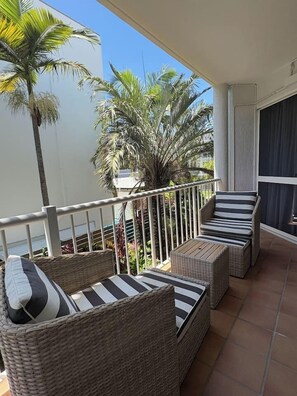 A balcony with wicker furniture and a view of palm trees.