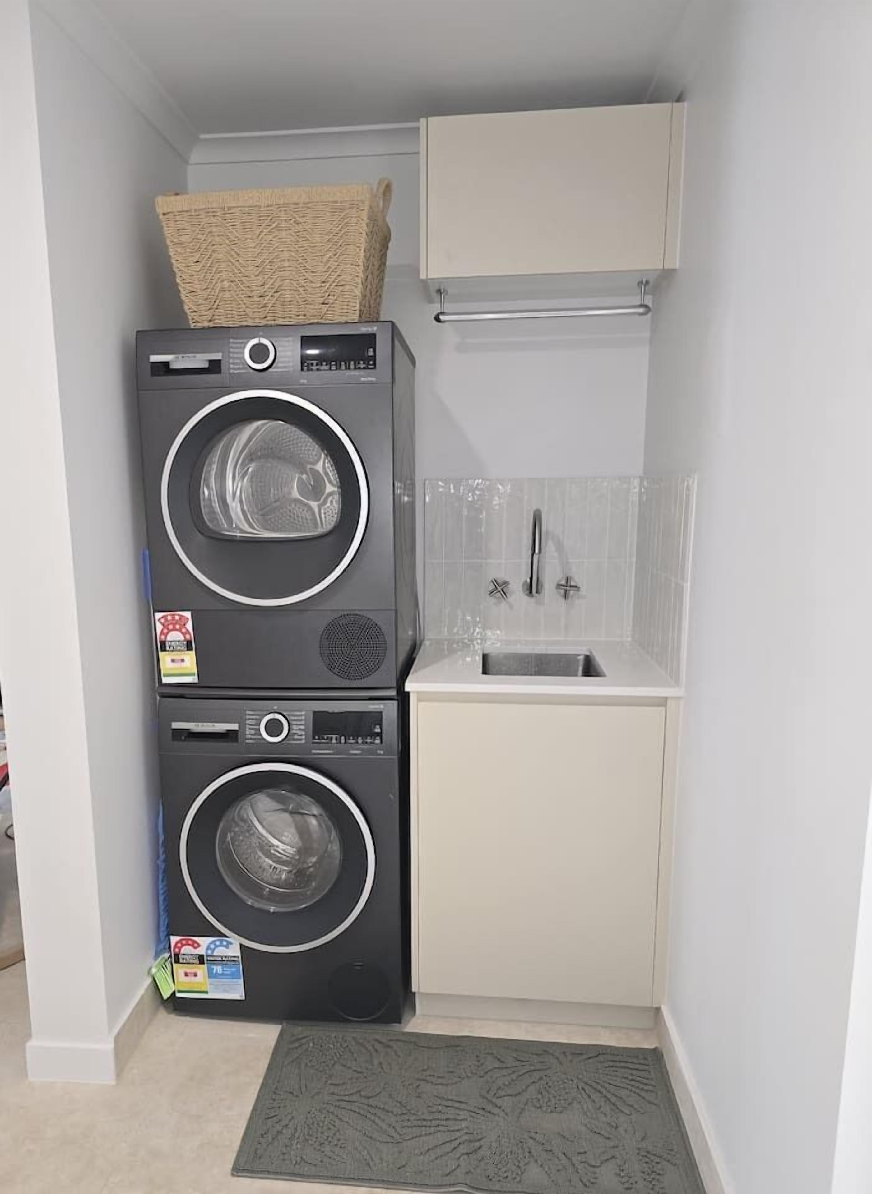 A compact laundry room with two stacked washing machines, a small sink, and a cabinet above.