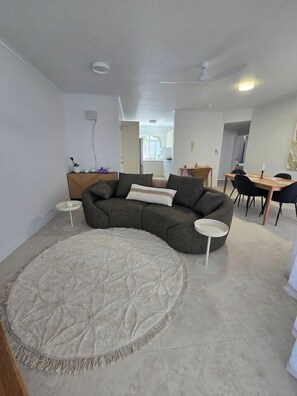 A living room with a grey sectional sofa, a round rug, a dining table with chairs, and a ceiling fan.