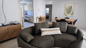 Una sala de estar moderna con un sofá seccional curvo, una mesita redonda y un comedor con una mesa y sillas de madera.