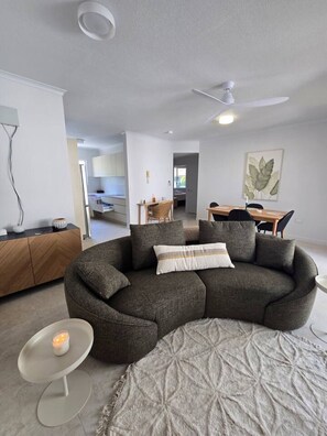 A modern living room with a curved sectional sofa, a small round coffee table, and a dining area with a wooden table and chairs.