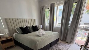 A bedroom with a bed, nightstands, a chair, a ceiling fan, and a view of the outside.