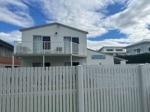 Un bâtiment à deux étages doté d’un balcon, d’une enseigne indiquant « Park Royale », et d’une clôture blanche en bois devant.
