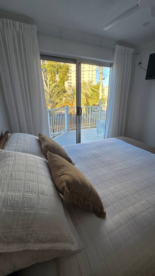 Une chambre à coucher avec un lit, des rideaux blancs et une vue sur un balcon doté d’une balustrade.