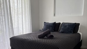 A bedroom with a bed, a window with sheer curtains, and a wall-mounted air conditioning unit. - Walk to the beach - 3 Bed-2 carparks in North Ward (North Ward)