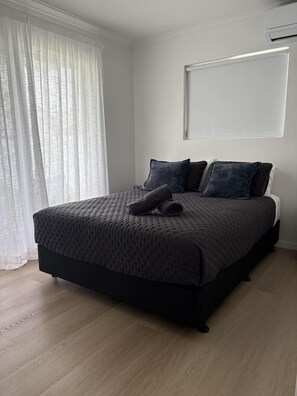 A bedroom with a bed, a window with sheer curtains, and a wall-mounted air conditioning unit. - Walk to the beach - 3 Bed-2 carparks in North Ward (North Ward)