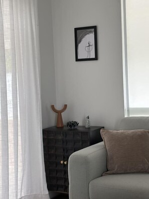 A living room with a grey sofa, a brown cushion, a black cabinet, and a framed picture on the wall. - Walk to the beach - 3 Bed-2 carparks in North Ward (North Ward)