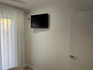 Une pièce dotée d’un téléviseur à écran plat fixé au mur, d’une porte et d’une fenêtre ornée de rideaux légers.