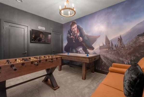 Ein Zimmer mit einem Kicker, einem großen Poster eines Zauberers und einem Sofa.