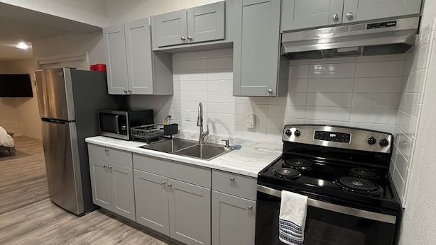 A modern kitchen with grey cabinets, stainless steel appliances, and a tiled backsplash.
