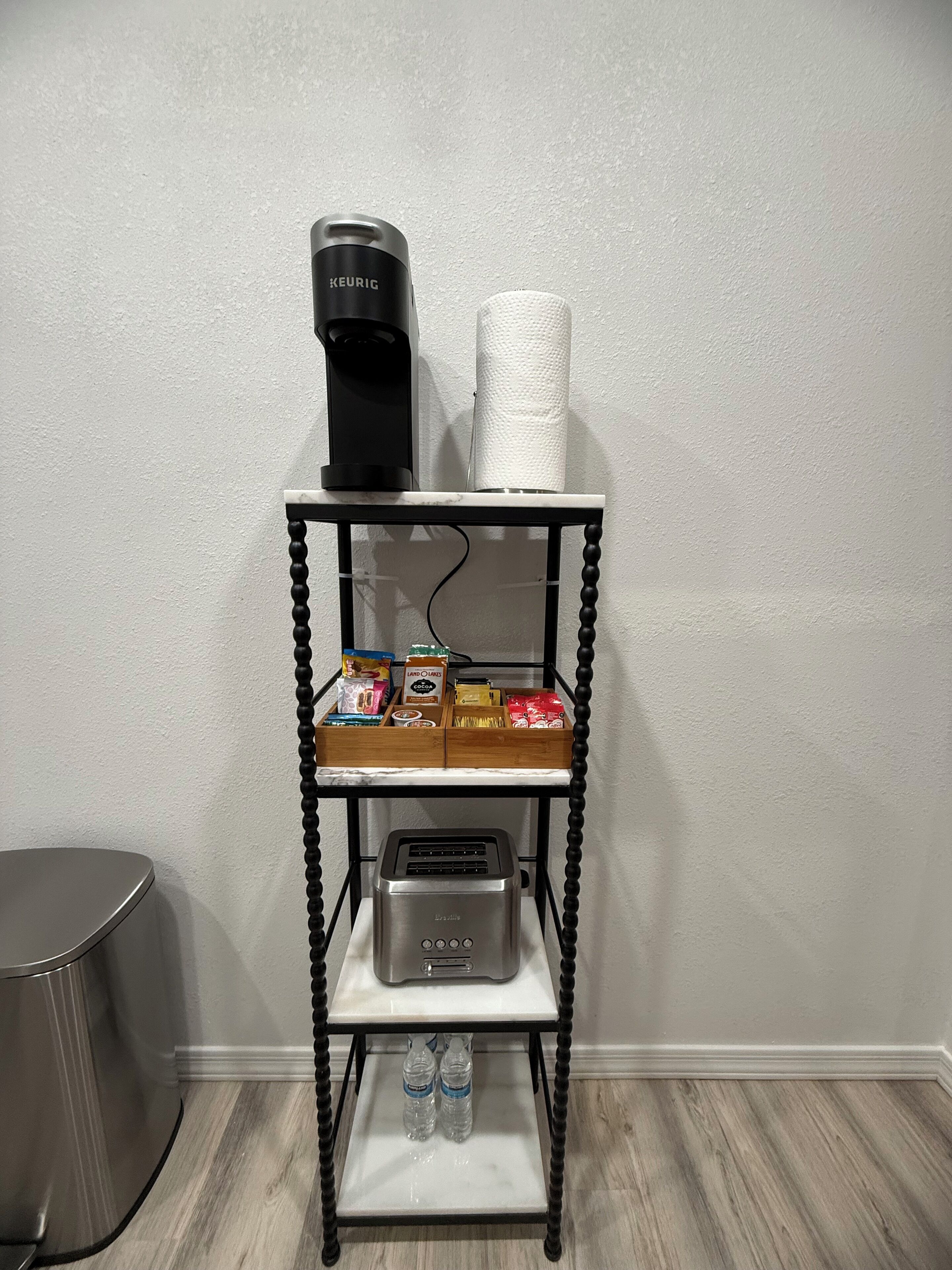 Un comptoir de cuisine avec une machine à café, un porte-essuie-tout et un grille-pain. On y trouve divers aliments et deux bouteilles d’eau.