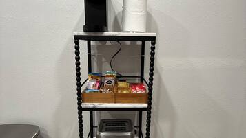 Un comptoir de cuisine avec une machine à café, un porte-essuie-tout et un grille-pain. On y trouve divers aliments et deux bouteilles d’eau.