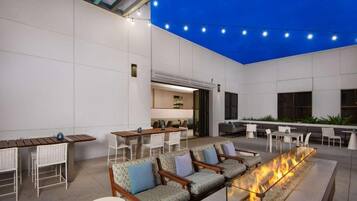 Un espacio lounge exterior moderno con asientos, una chimenea y luces colgantes.