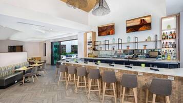 Zona de bar moderna con una barra larga, taburetes y un espacio de estar con sofá y mesas.