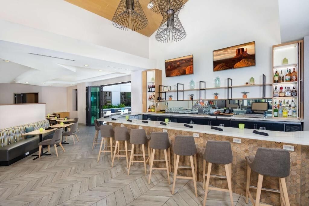 Zona de bar moderna con una barra larga, taburetes y un espacio de estar con sofá y mesas.