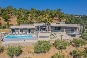 Una casa moderna de dos pisos amb piscina, mobiliari exterior i vistes a un paisatge amb pujols.