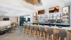 A modern bar area with a long counter, bar stools, and a seating area with a sofa and tables.
