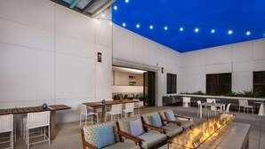 Un espace de détente extérieur moderne, doté de sièges, d’un foyer et de guirlandes lumineuses.