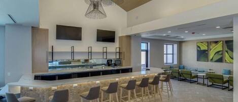 A modern kitchen with a central island, bar stools, and a seating area with green upholstered chairs.