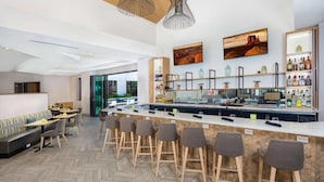 Zona de bar moderna con una barra larga, taburetes y un espacio de estar con sofá y mesas.