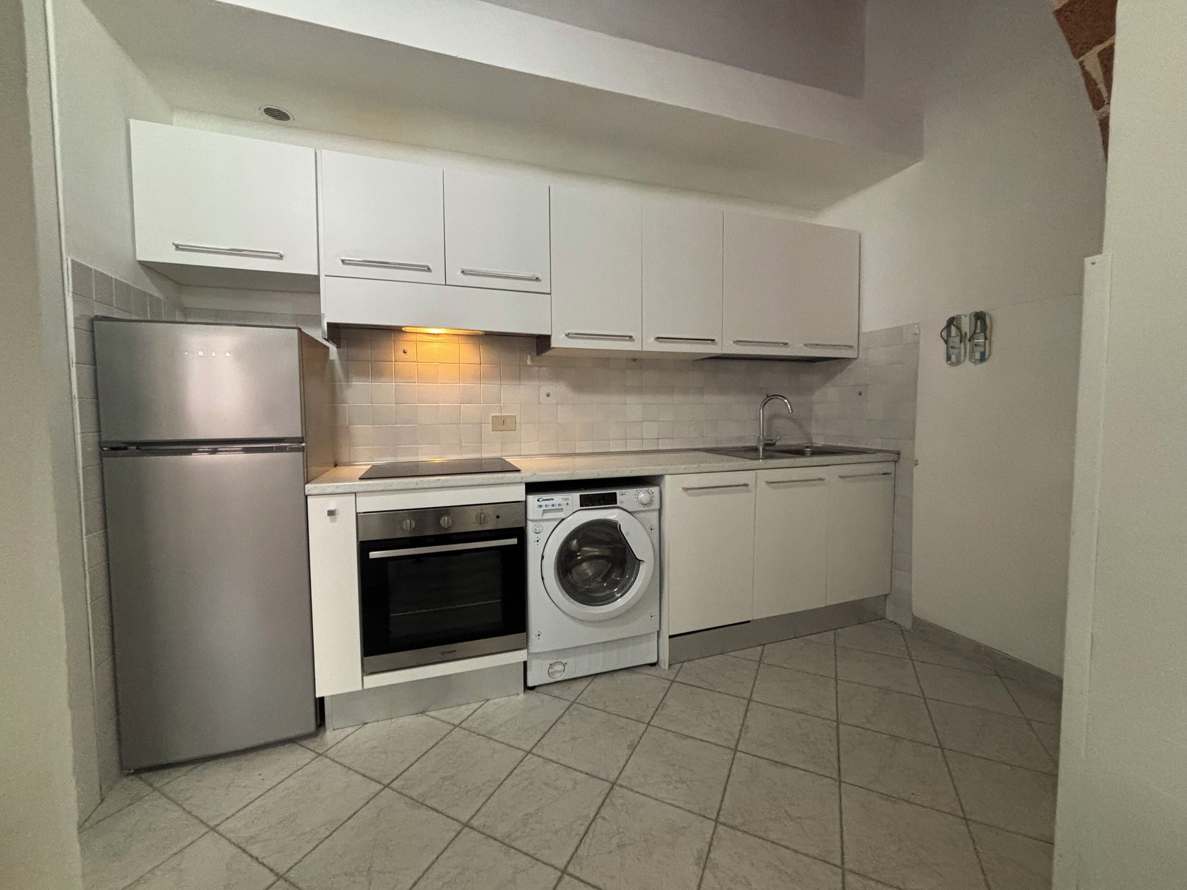 A compact kitchen with a refrigerator, oven, washing machine, and a sink.
