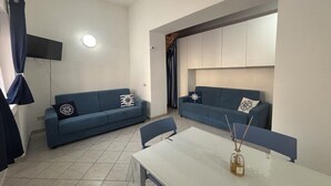 Ein modernes Wohnzimmer mit zwei blauen Sofas, einem weißen Tisch und einem an der Wand montierten Fernseher.