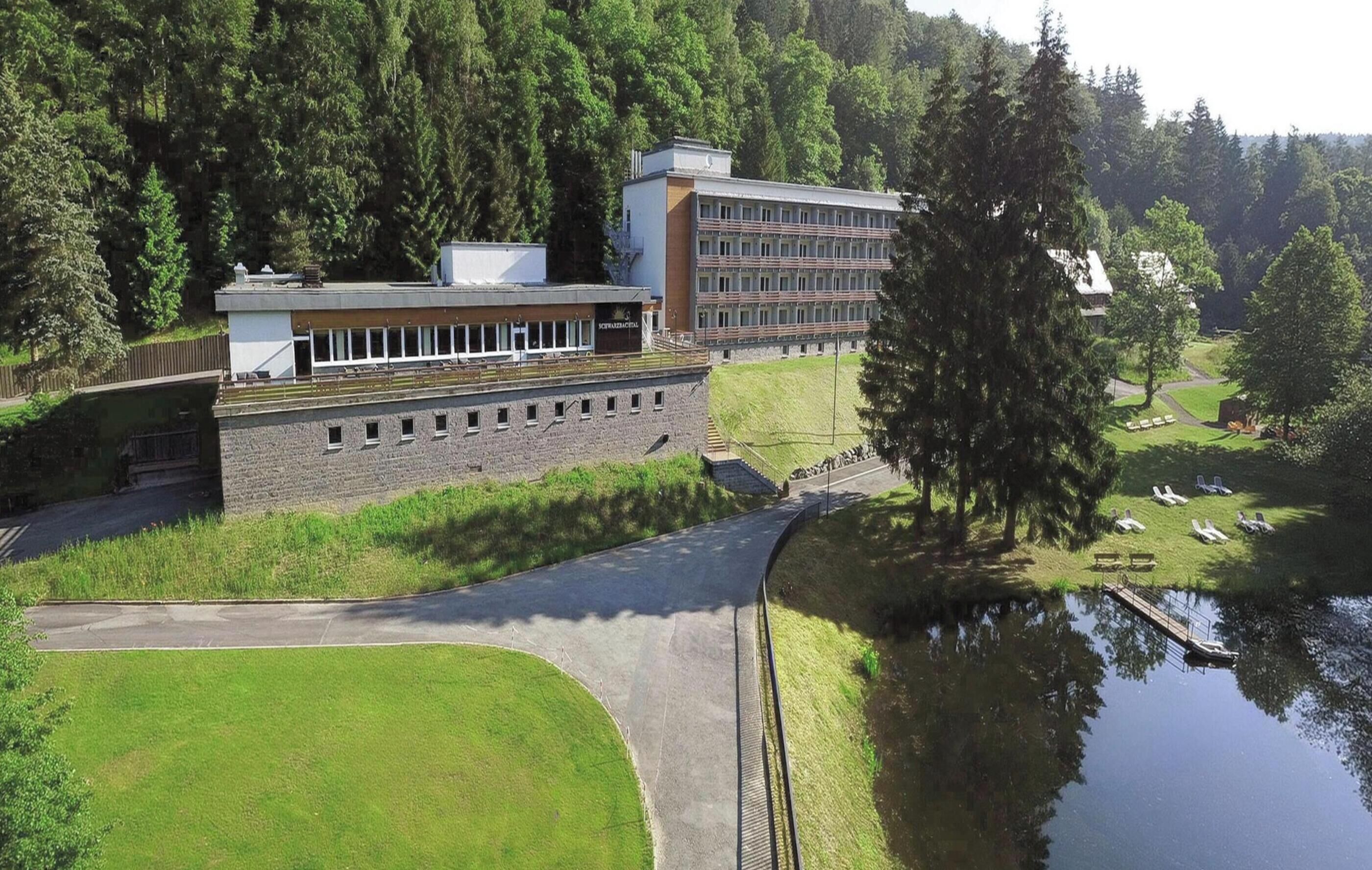 Un edificio moderno con tetto piano, un'ampia vetrata e una zona verde con uno stagno.