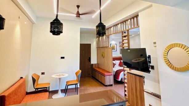 A modern hotel room with a wooden ceiling, a dining area with orange chairs, a TV, and a circular wall decoration. - J&G Royal Stay- A Boutique Hotel (Kanayannur)